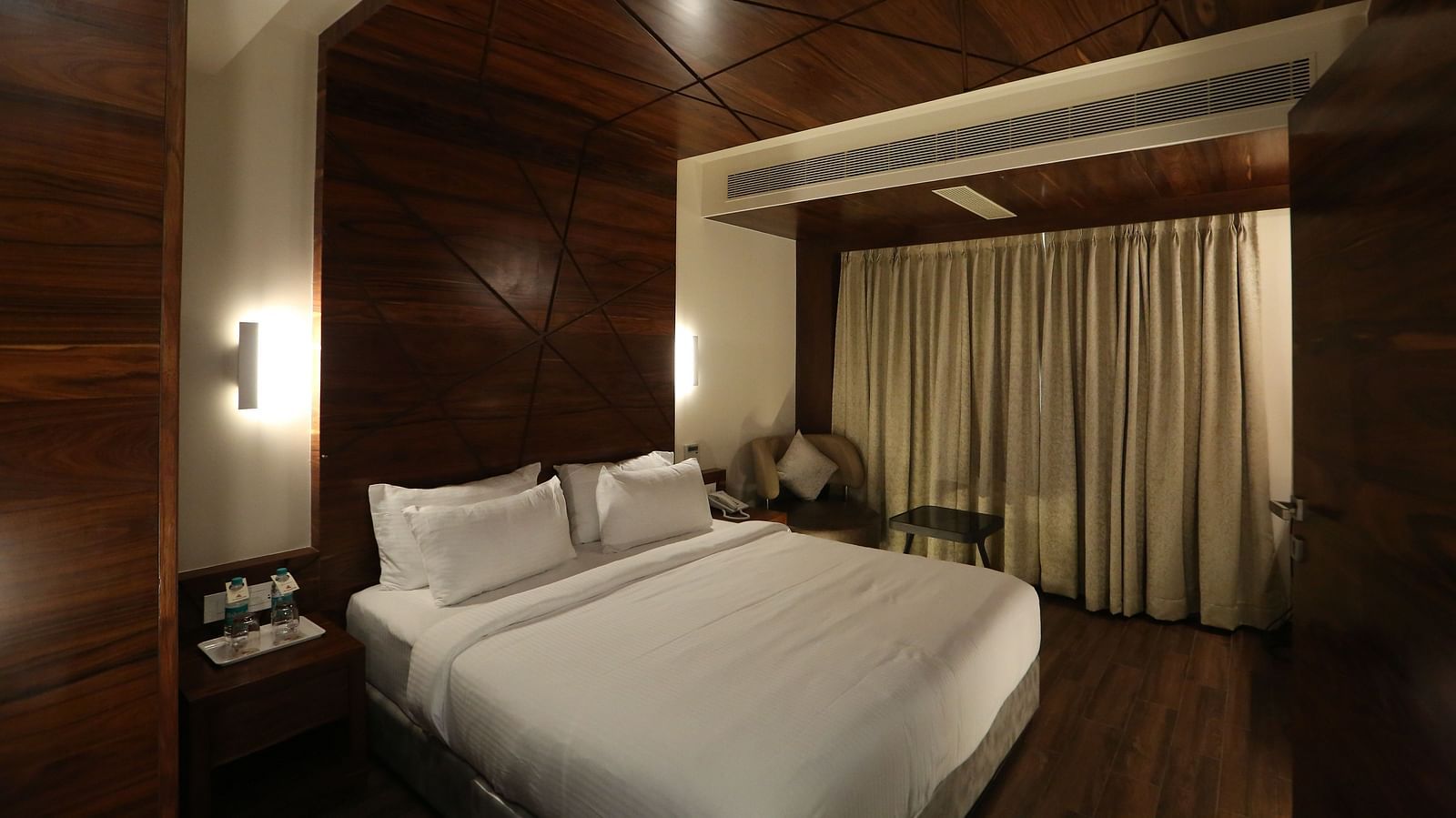 Premium Suite featuring a king size bed, bedside tables, lamps, and dark wood panelling - TGI SPS Grand, Coimbatore