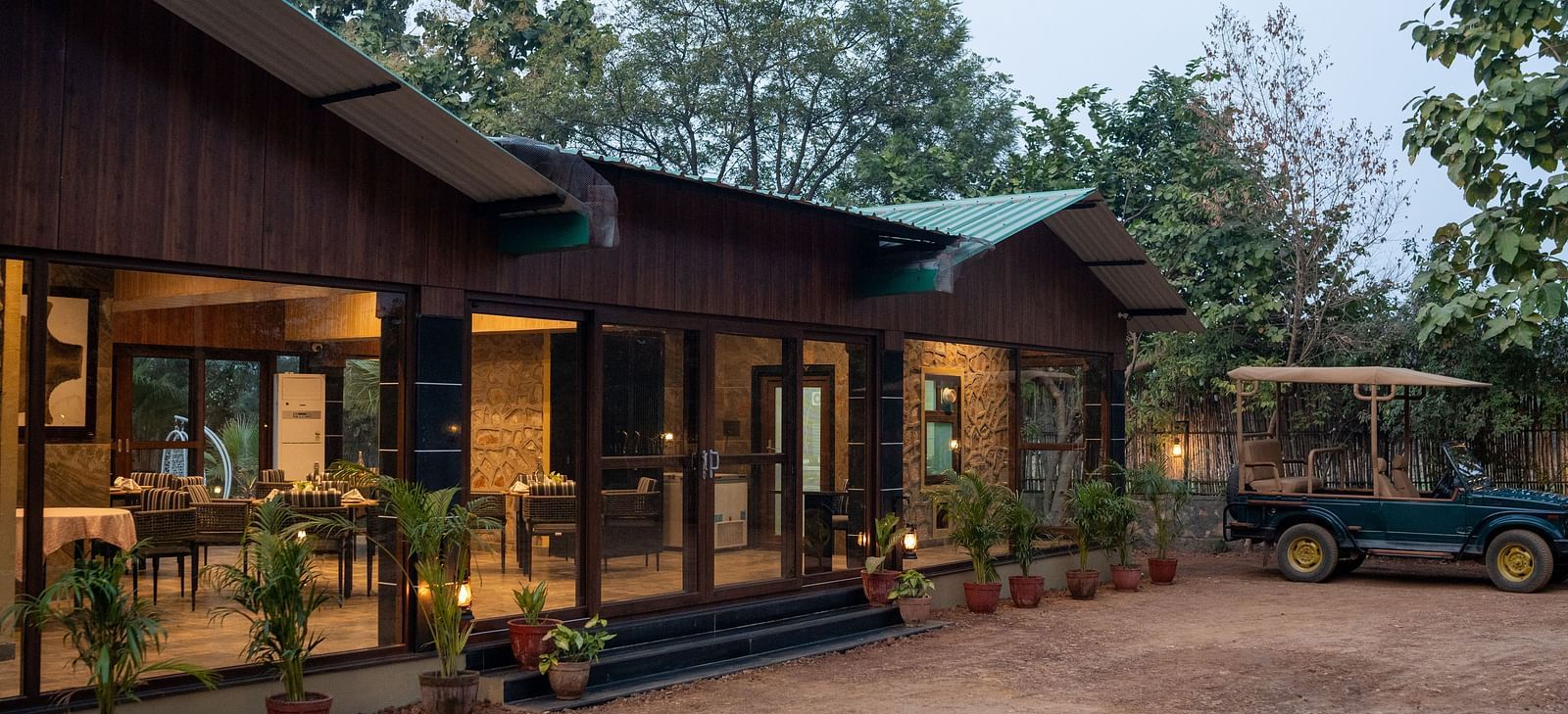 At Aamaghati Jungle Retreat, Ranthambore, the main building features modern architecture with expansive windows, and a safari jeep is parked nearby.