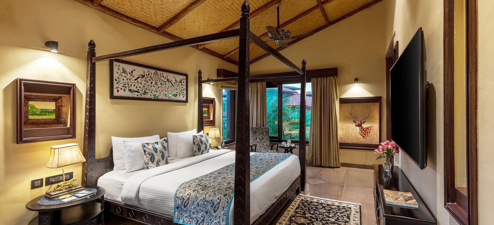 A luxurious bedroom with a large bed, blue accents, and wooden ceiling at Aamaghati Wildlife Resort.