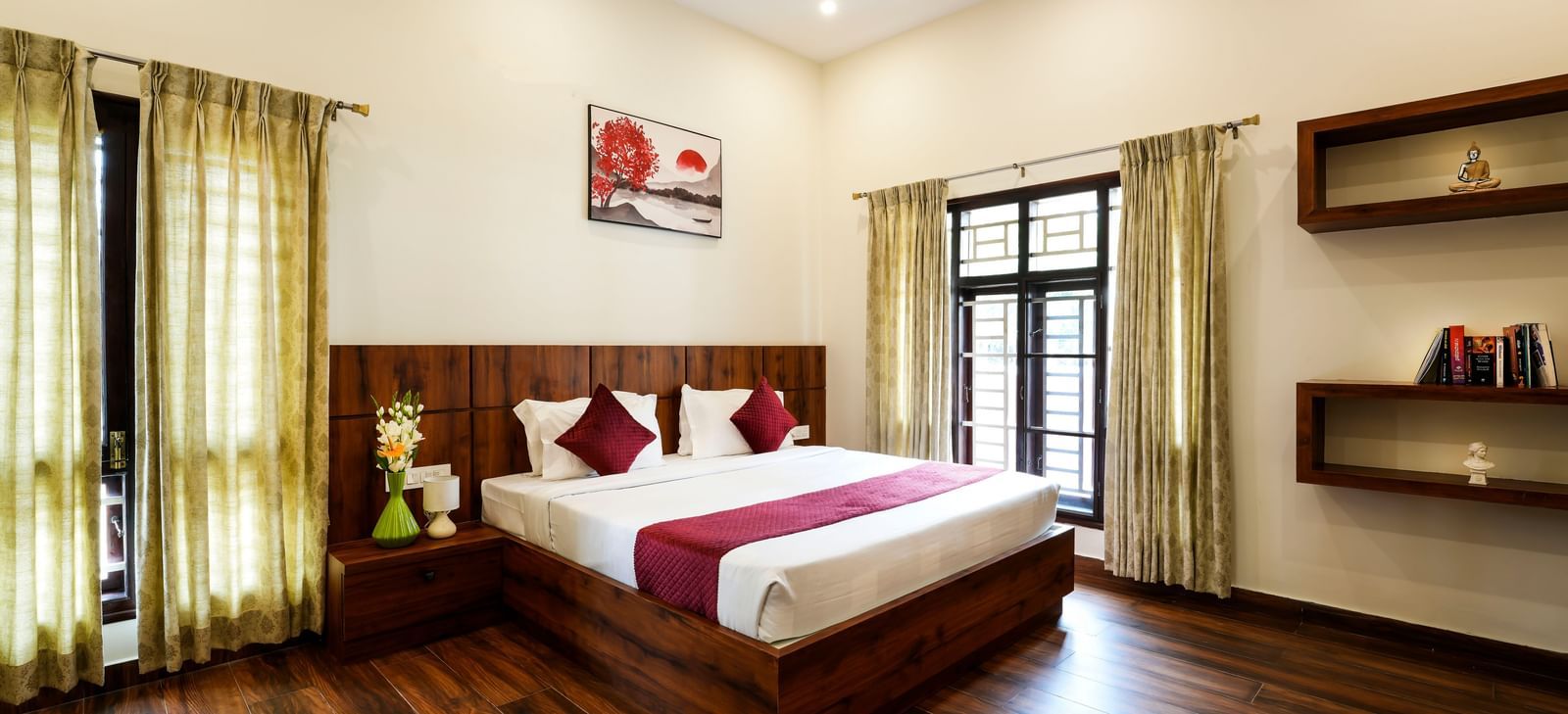  A spacious deluxe room at Bhuthanakadu Retreat, featuring a large bed with a rich wooden headboard, a red and white duvet, and warm recessed lighting.