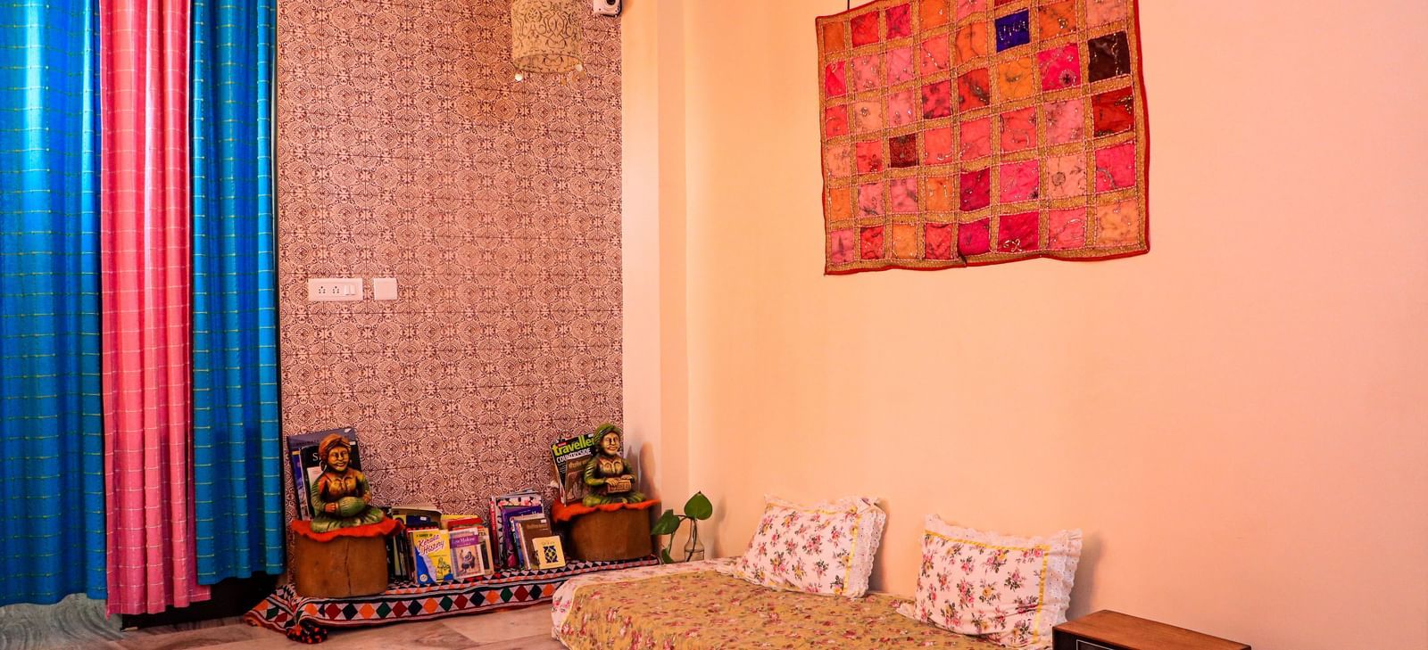 A room with a low bed, cushions, wall hanging, floor seating, and decorative elements on shelves at Jaypore360 Homestay in Jaipur.