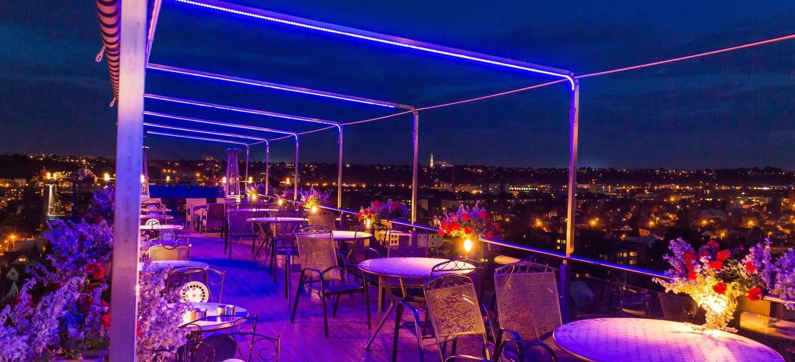 A rooftop terrace bar at night with glowing neon lights and outdoor seating.