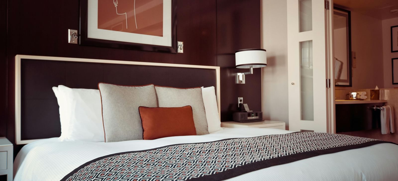 A hotel bedroom with a large bed, crisp white linen, and a cushioned headboard.