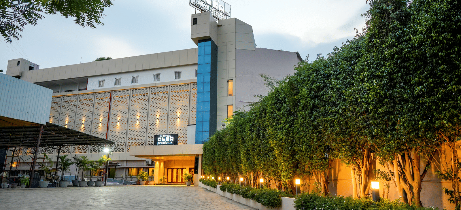 Exterior view of hotel building with driveway and trees at Pravasa Hotel, Kolhapur.