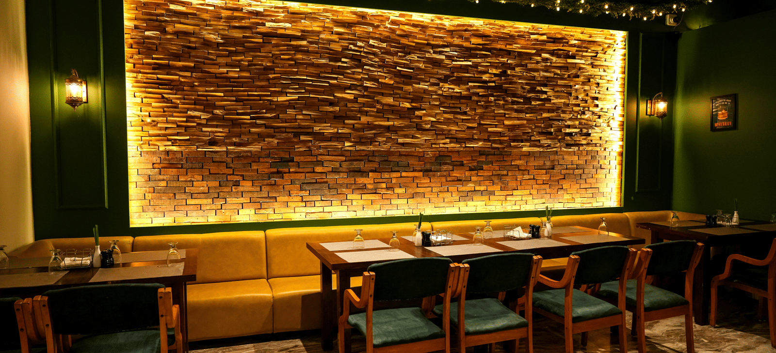  A warm dining section with a long yellow upholstered booth and a dramatic backlit stone feature wall at Pravasa Hotel, Kolhapur.
