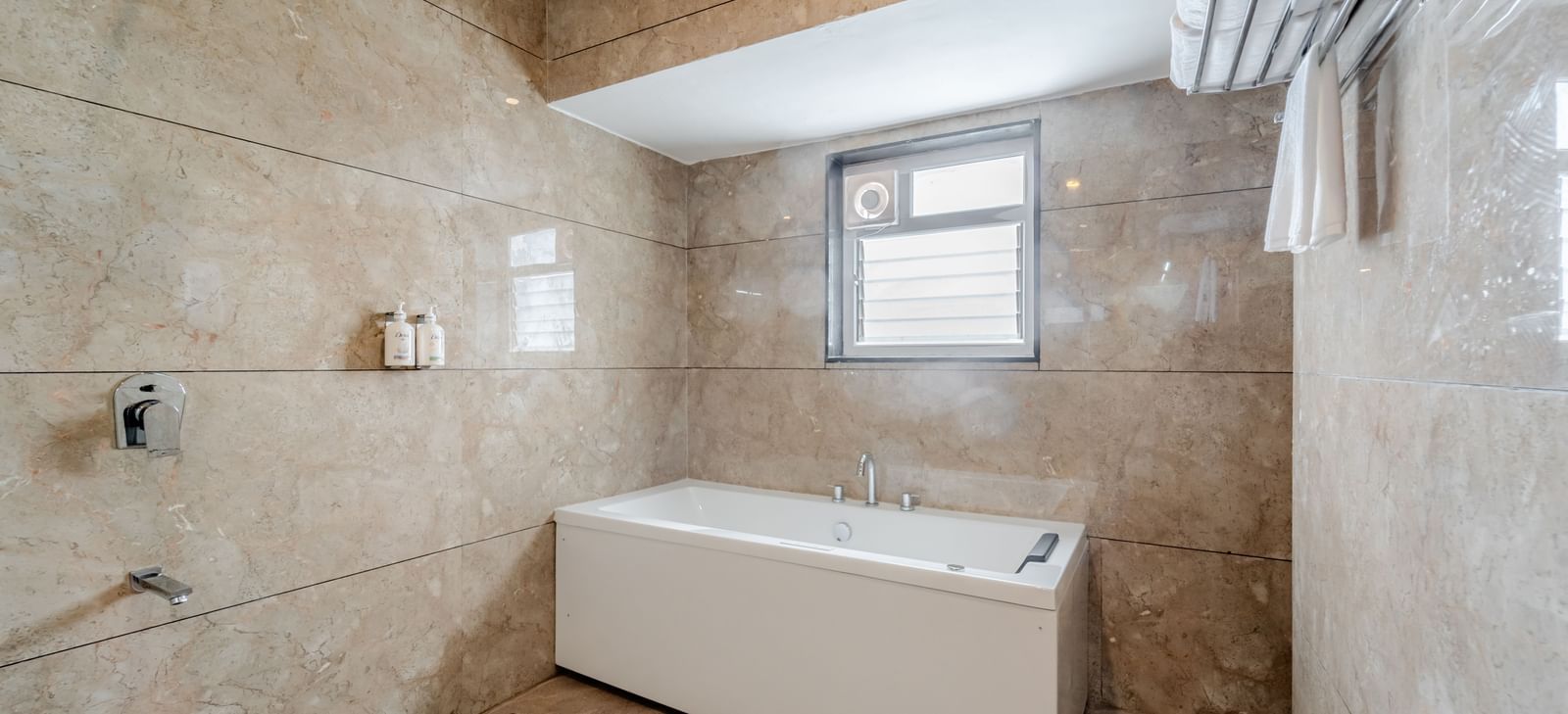 A suite bathroom with a white bathtub and patterned beige tiles | Suite | Pravasa Hotel, Vijayapura
