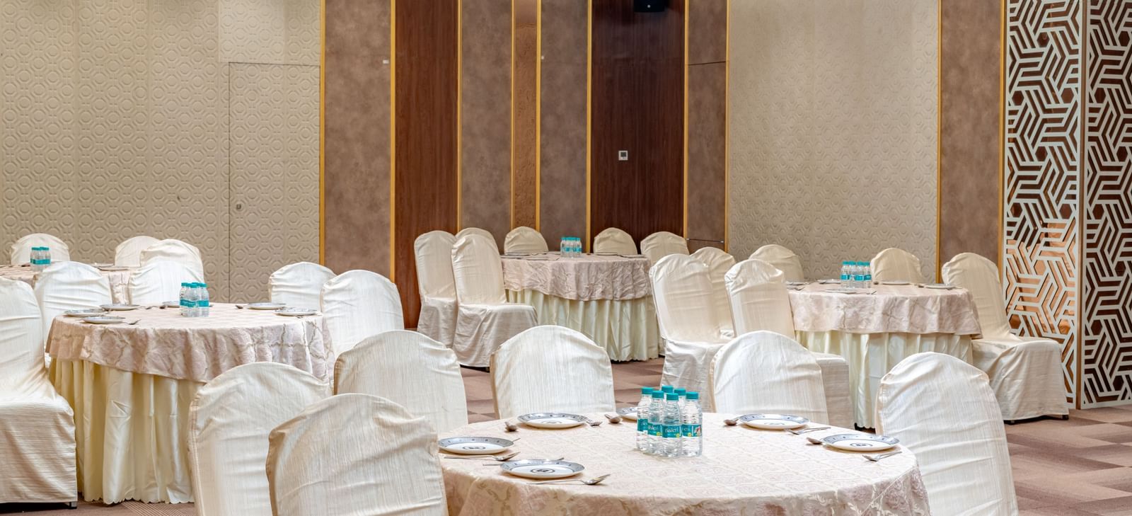 A banquet hall with round tables and elegant chairs | Meetings & Events | Pravasa Hotel, Vijayapura