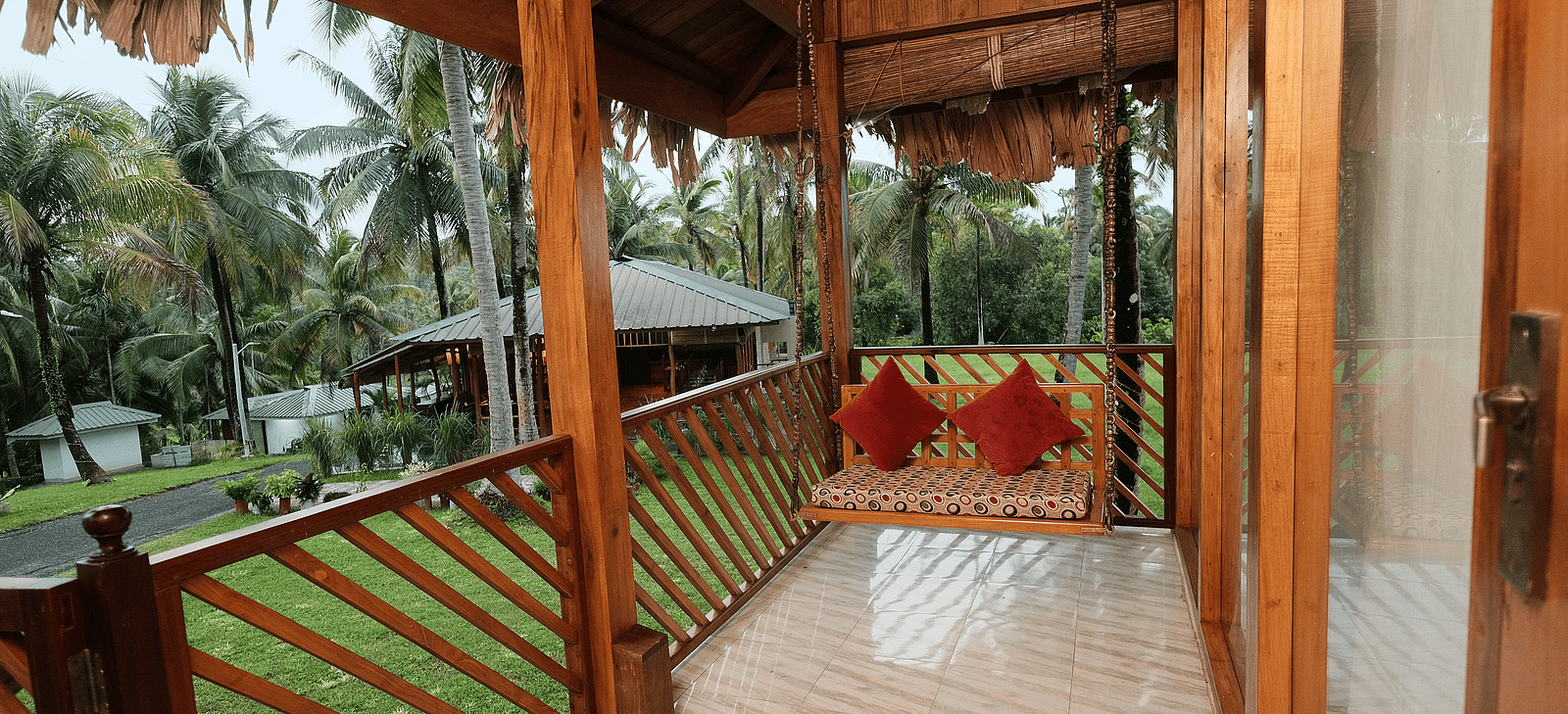 A close-up of a rustic wooden gazebo or porch with a thatched roof, featuring red cushions on a swing seat.