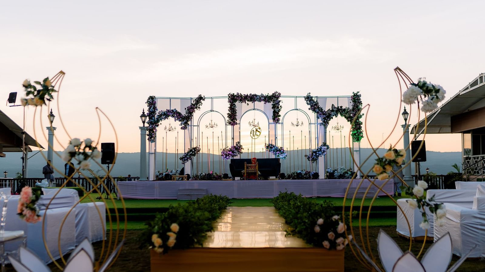 An outdoor wedding stage and walkway are beautifully decorated with flowers and lights at sunset, awaiting the evening celebration - The Grand Legacy Resort and Spa