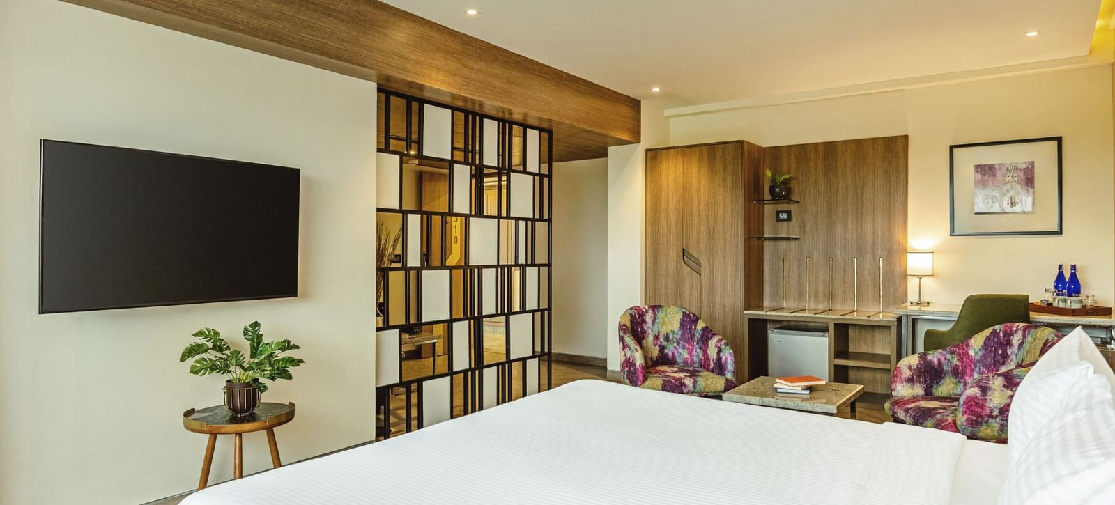  A wide-angle view of a room with a large bed and a television at Mango Hill Central, Chennai. A desk and chair are on the left.