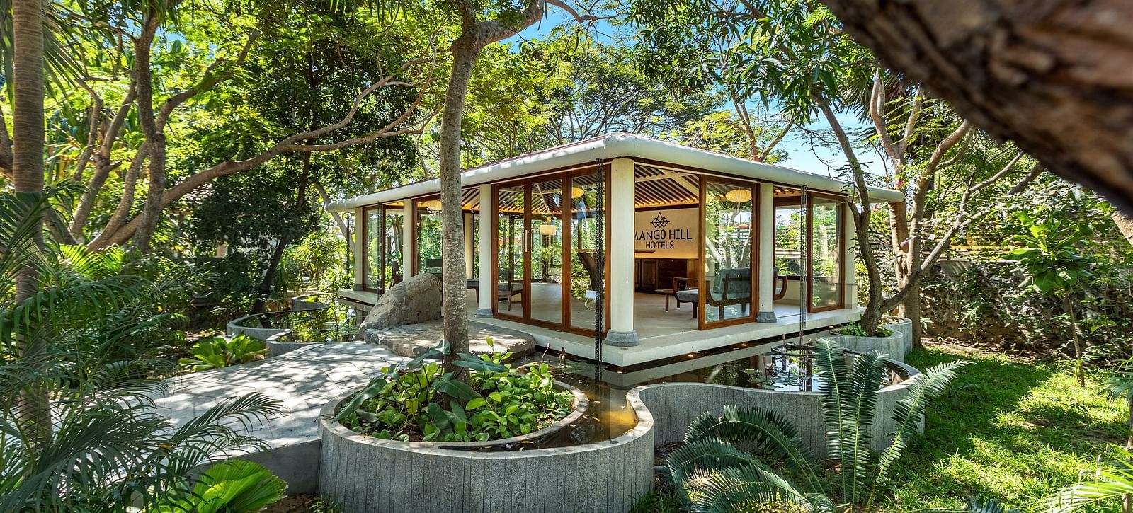 Modern glass-walled building surrounded by lush greenery | Mango Hill Shallow Beach Resort ECR