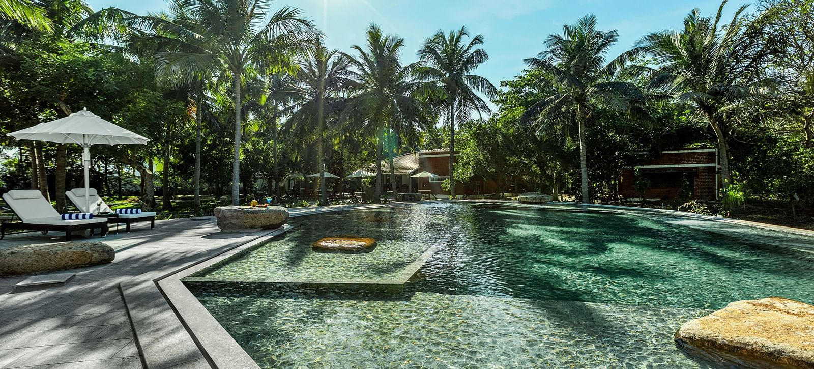 Resort swimming pool with lounge chairs and palm trees under a sunny sky | Mango Hill Shallow Beach Resort ECR