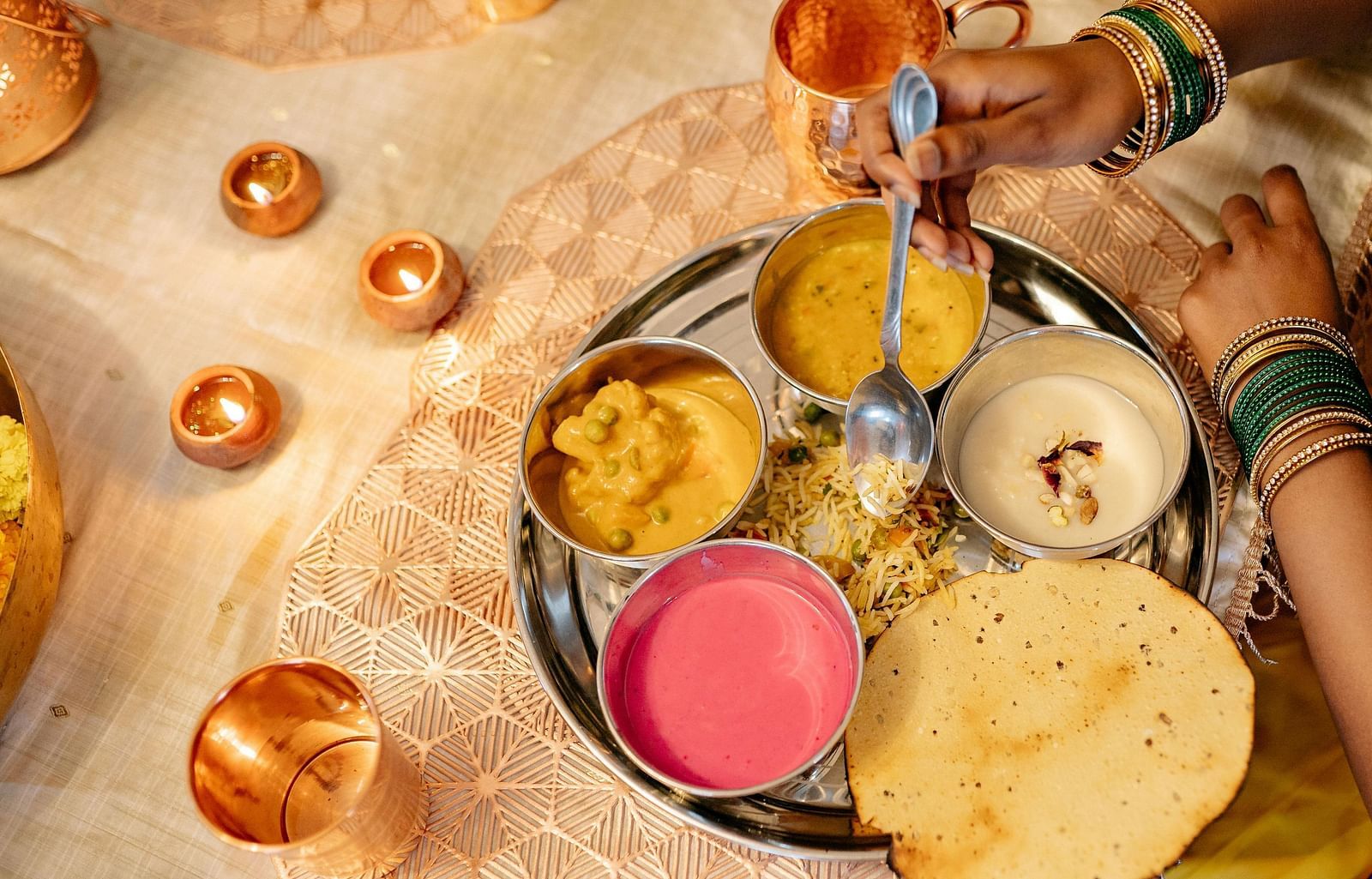 A woman is shown enjoying a traditional Indian thali meal, featuring various dishes served in small bowls arranged on a round platter.