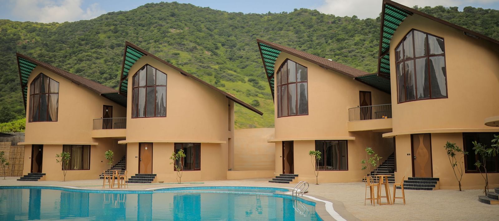 The Qualia Resort Club & Brewery, Udaipur presented with a long pool and lush green mountains in the backdrop.