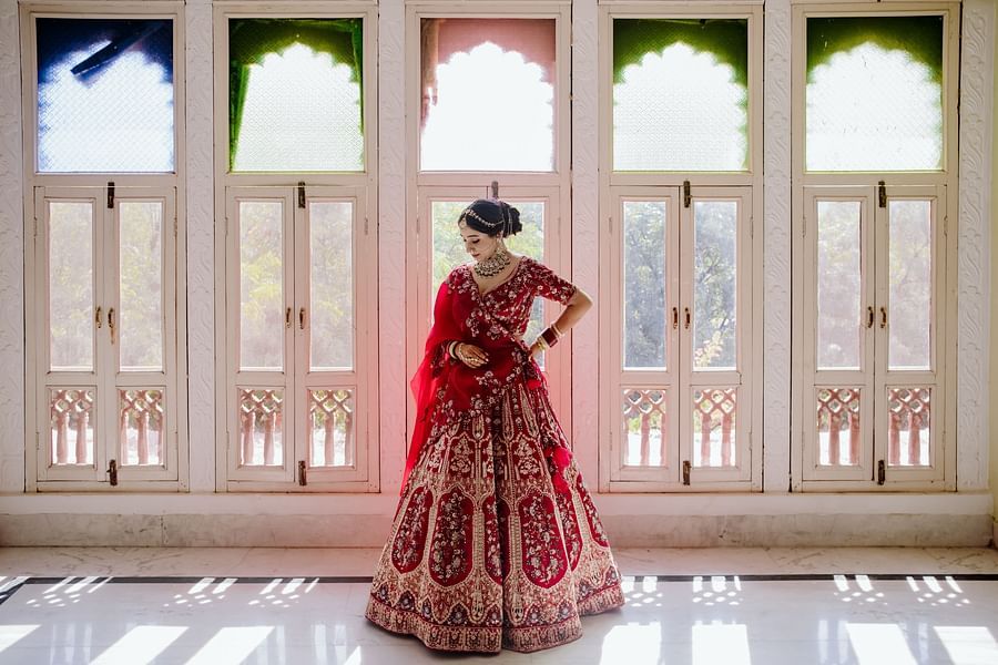 A bride poses by a window, wearing a lehenga and traditional jewelry - Umaid Palace - Best Luxury Heritage Resort Near Jaipur. 