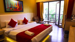 A bright hotel room with a yellow accent wall and a queen bed dressed with white and red linens and towel art.