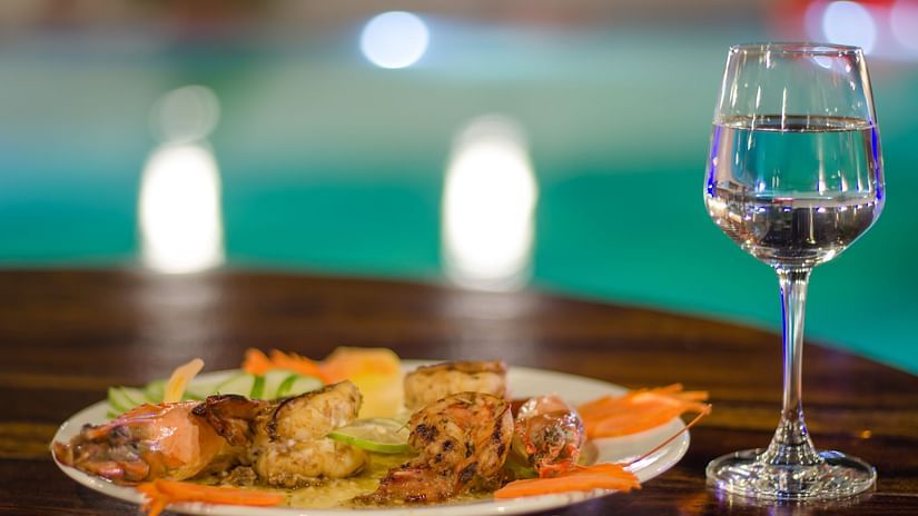 glass of water next to plate of food kept on a table with the swimming pool in the background - Symphony Summer Sand Beach Resort And Spa, Neil island