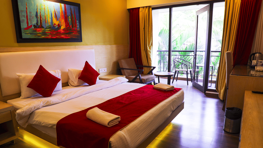 A bright hotel room with a yellow accent wall and a queen bed dressed with white and red linens and towel art.