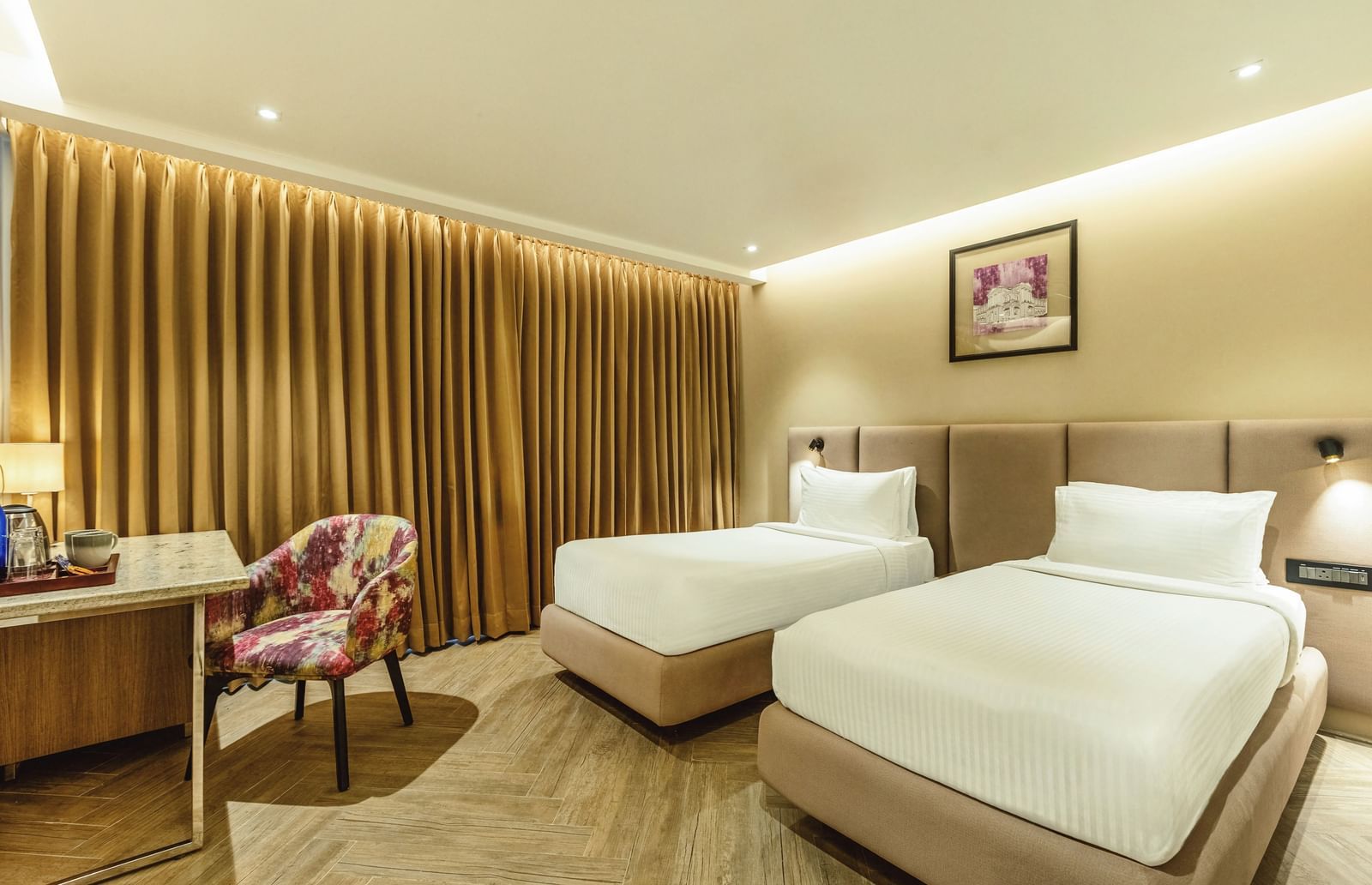 A wide shot of a twin-bedded room at Mango Hill Central, Chennai. A desk is on the left, and a wooden slat wall is behind the beds.
