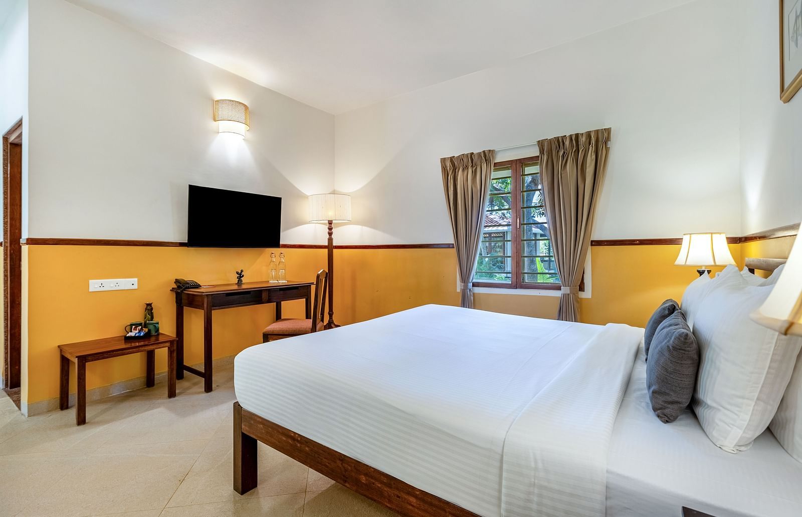 Well-lit bedroom with a wooden bed frame, white linens, a desk and chair, a flat-screen TV, and a window with drapes| Mango Hill Shallow Beach Resort ECR