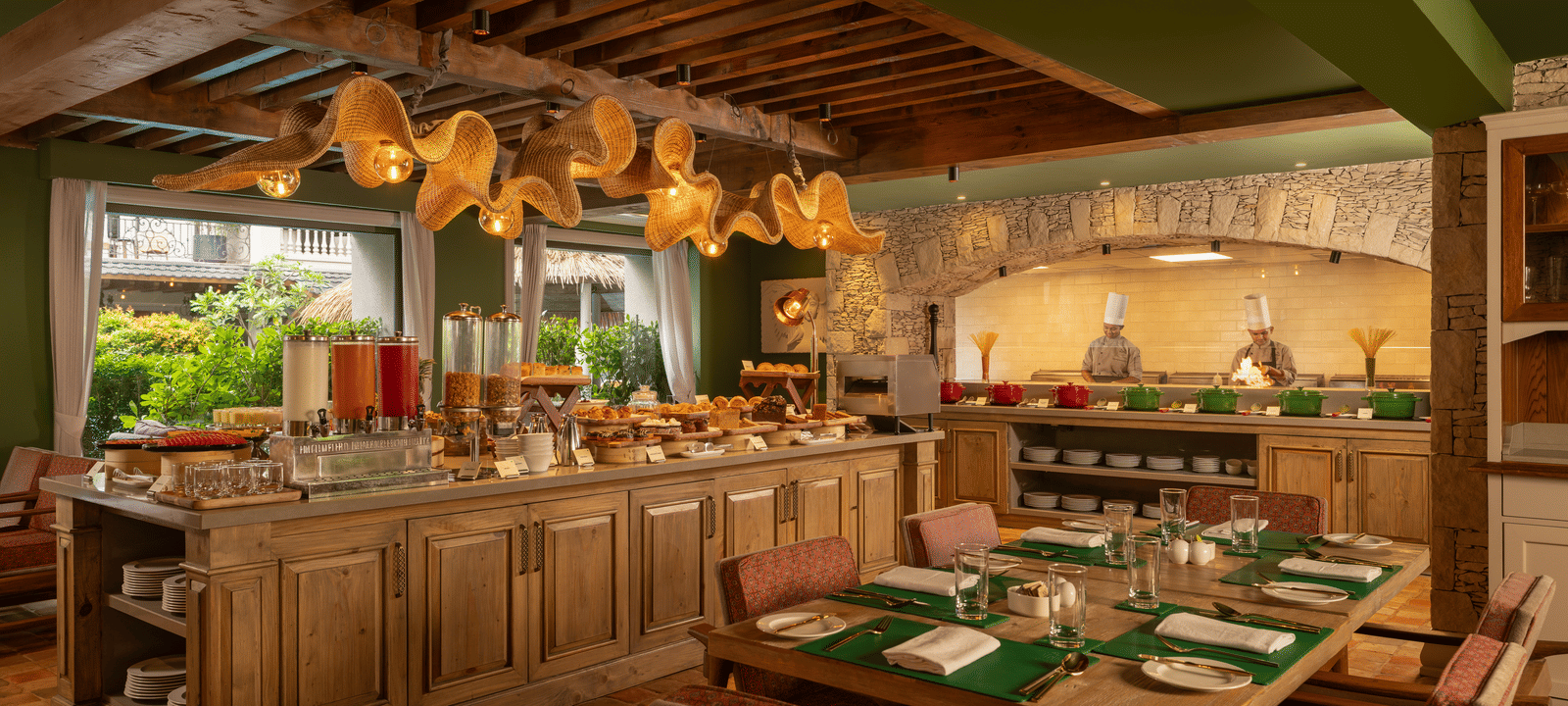 A wide-angle shot of Mila Restaurant at The Evren, Vagator, featuring a buffet counter in the middle of the dining area surrounded with well-arranged tables with cutlery and napkins.
