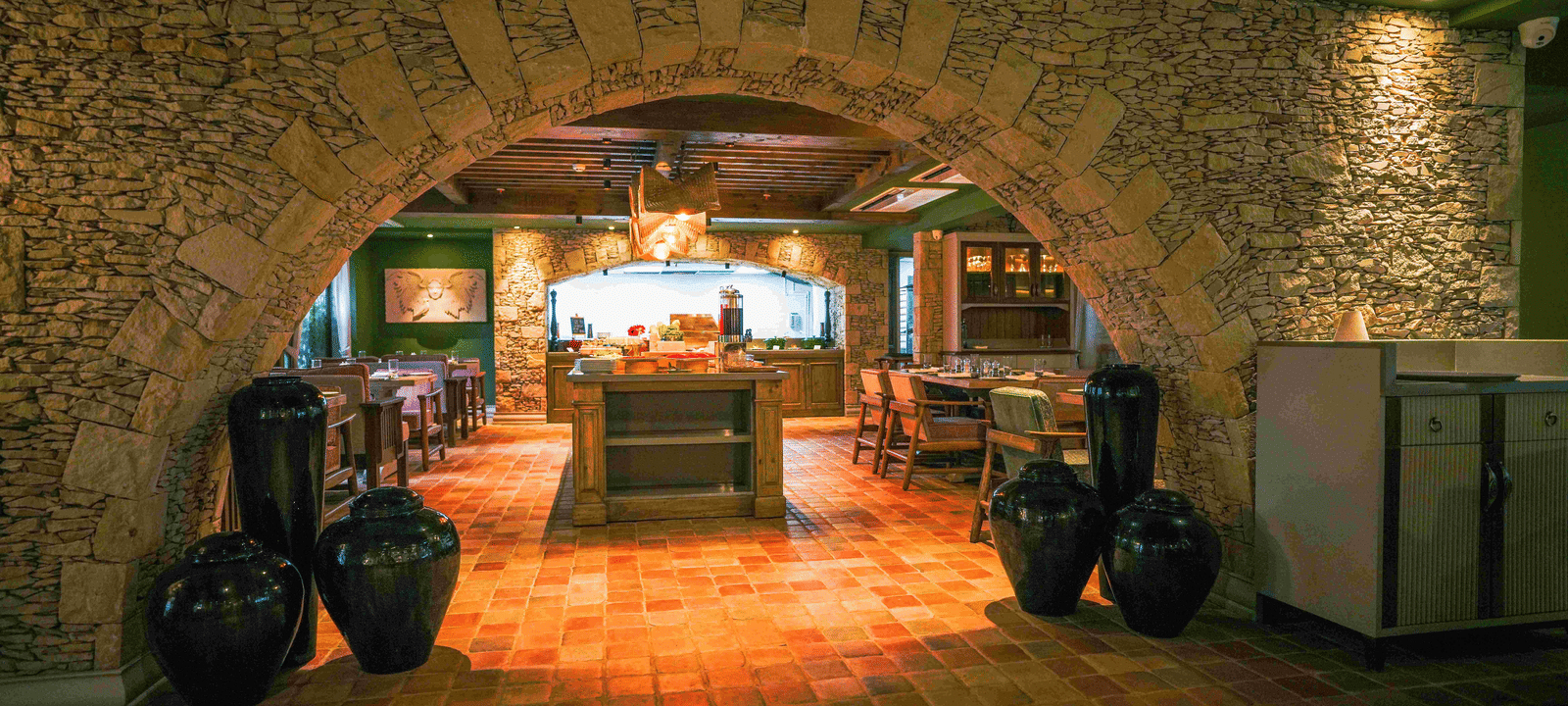 Front view of the Mila Restaurant at The Evren, Vagator, taken through a rustic stone archway featuring a tiled flooring along with well-arranged dining tables.