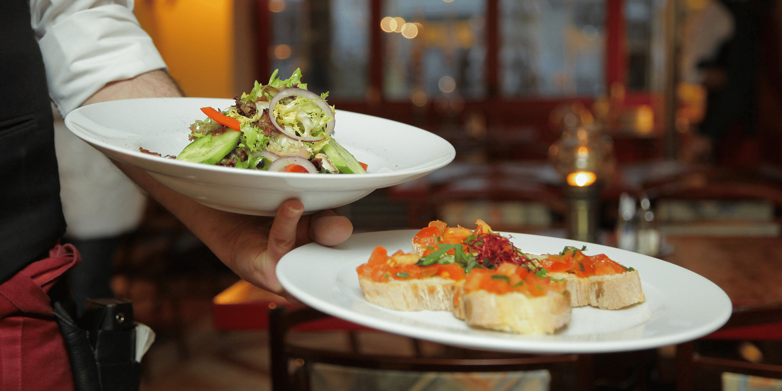 a person in a restaurant holding two plates with delicious cuisines in it that are well plated