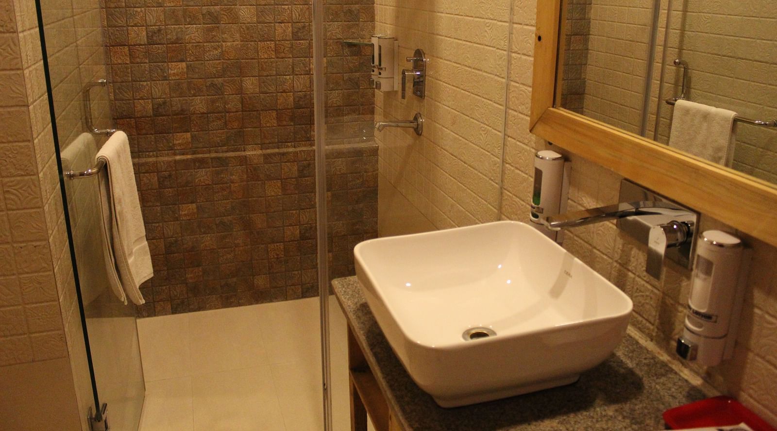 Modern bathroom with a glass shower, white sink, and large mirror at Dagshai Manor Kasauli - Inde Hotels.