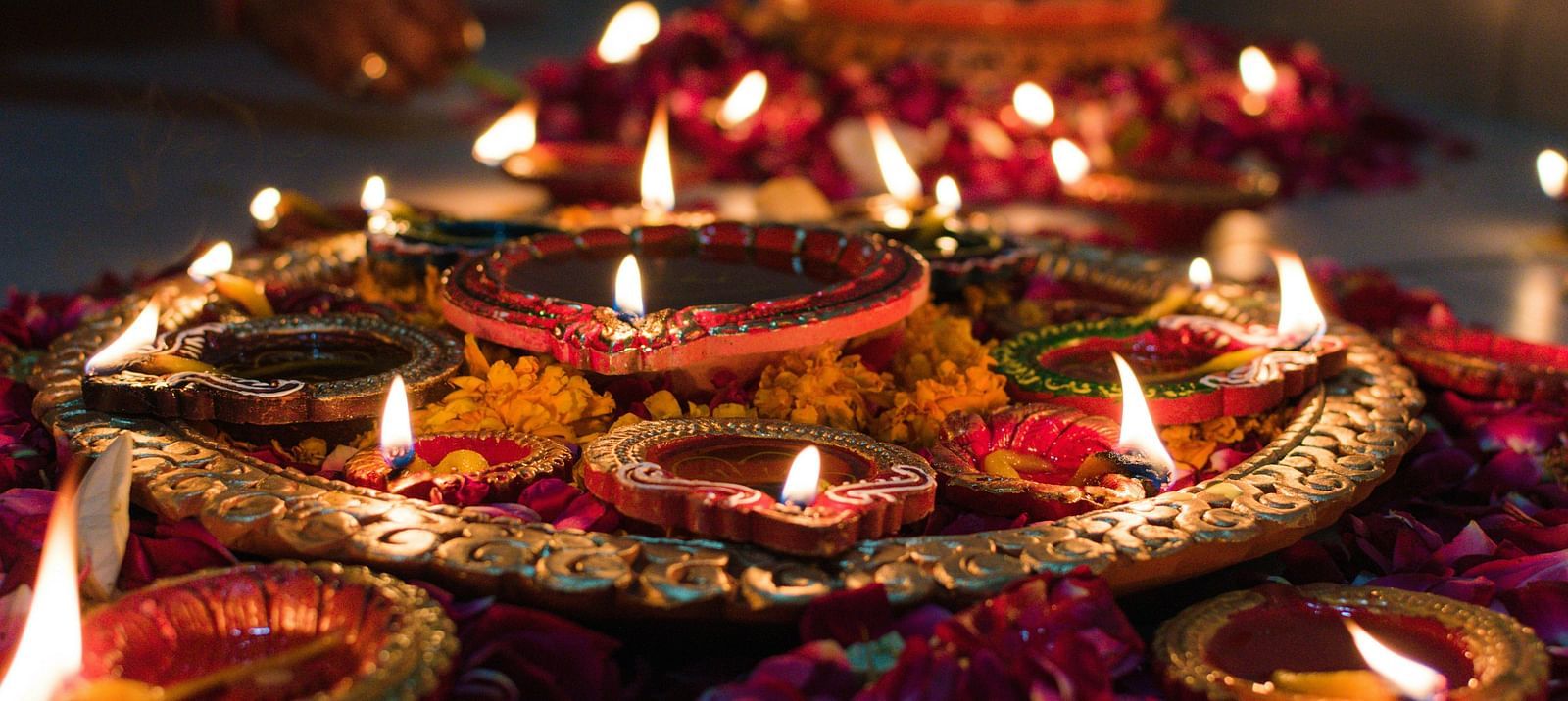 a close up image of a plate carrying several earthen lamps surrounded by flower petals