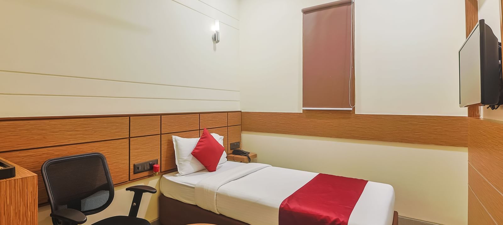 Bedroom with twin beds, red runners, pillows, chair and wall-mounted TV at Max Hotel Prayagraj.