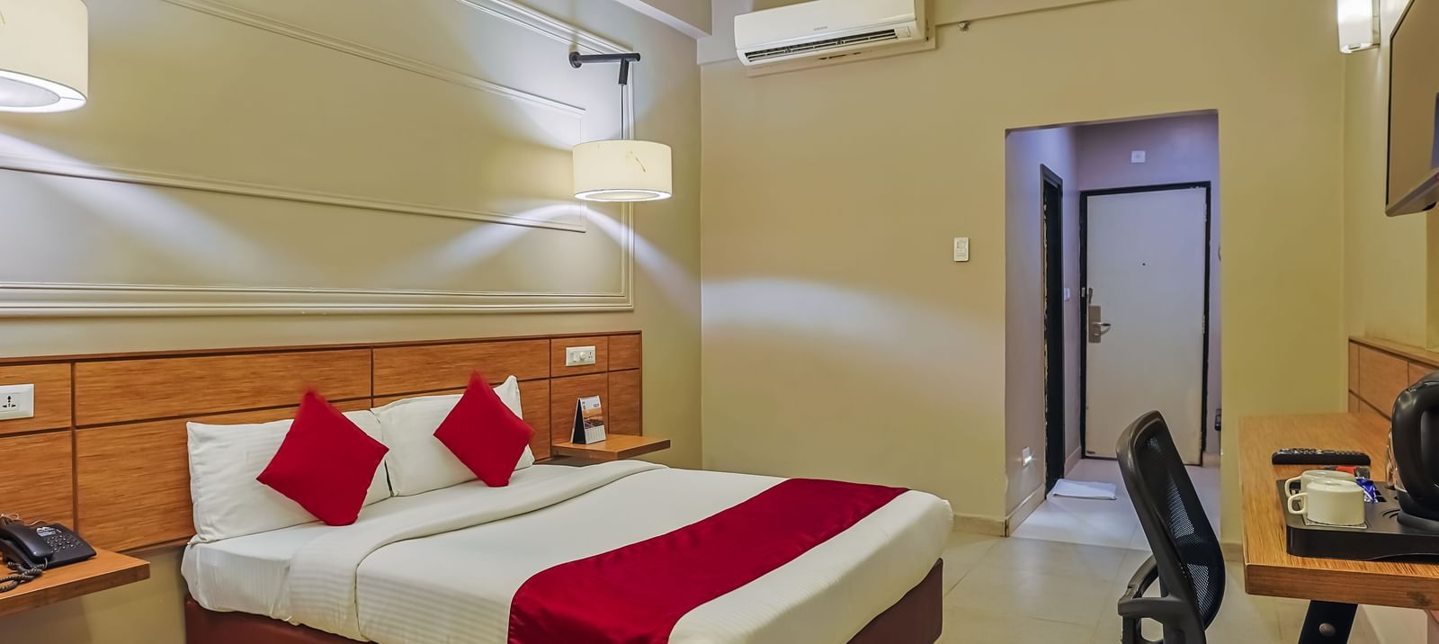 Bedroom with double bed, red runner, pillows, work desk and chair at Max Hotel Prayagraj.