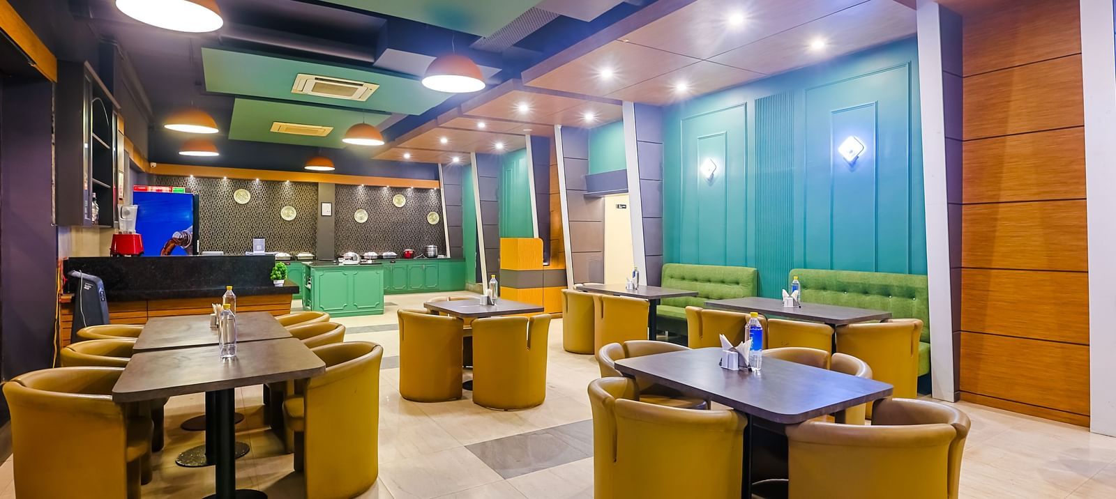 Restaurant dining area with round tables, cushioned chairs and lighting at Max Hotel Prayagraj.