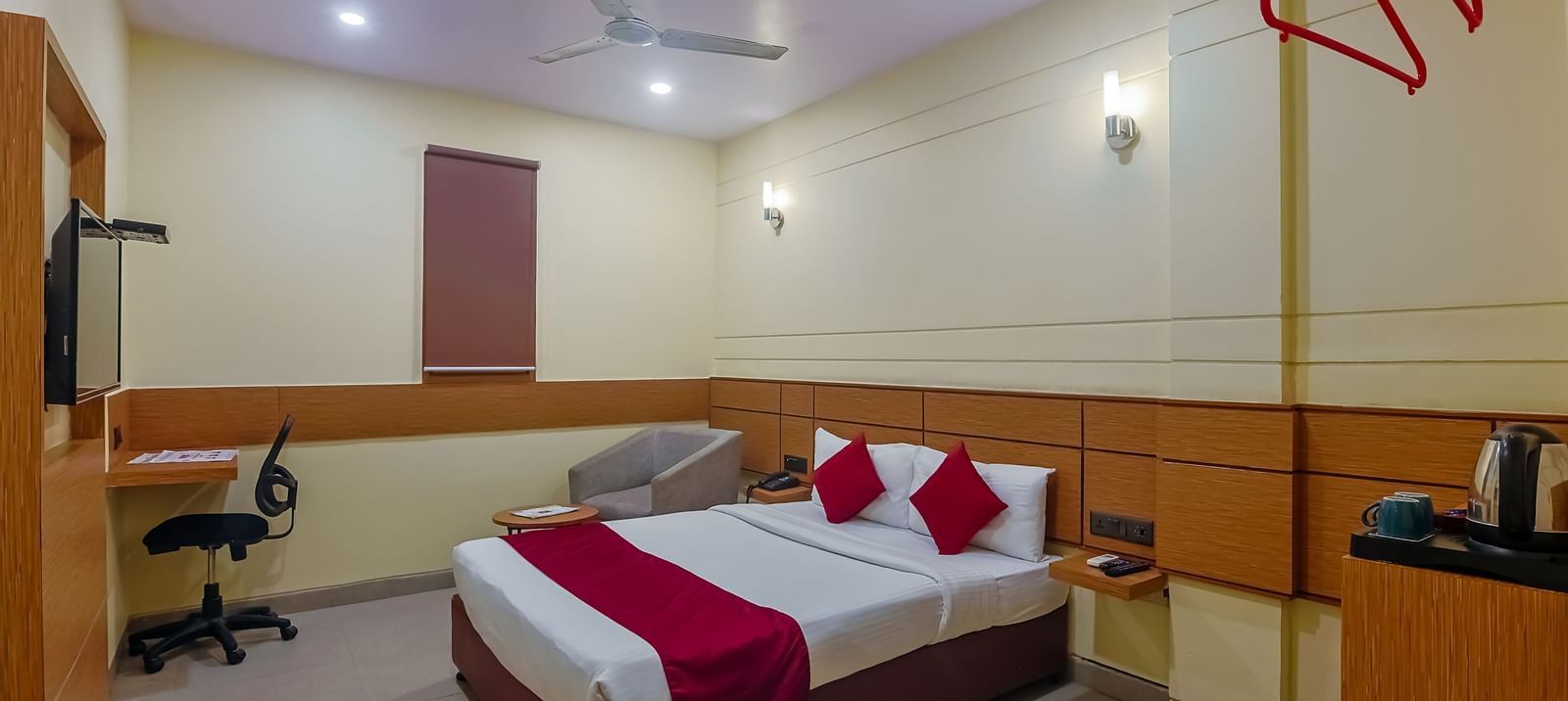 Bedroom with double bed, red runner, pillows, desk and wooden panel at Max Hotel Prayagraj.