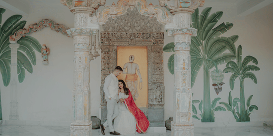 A couple standing against a decorated pillar in the hall at Fateh Vilas, Udaipur.