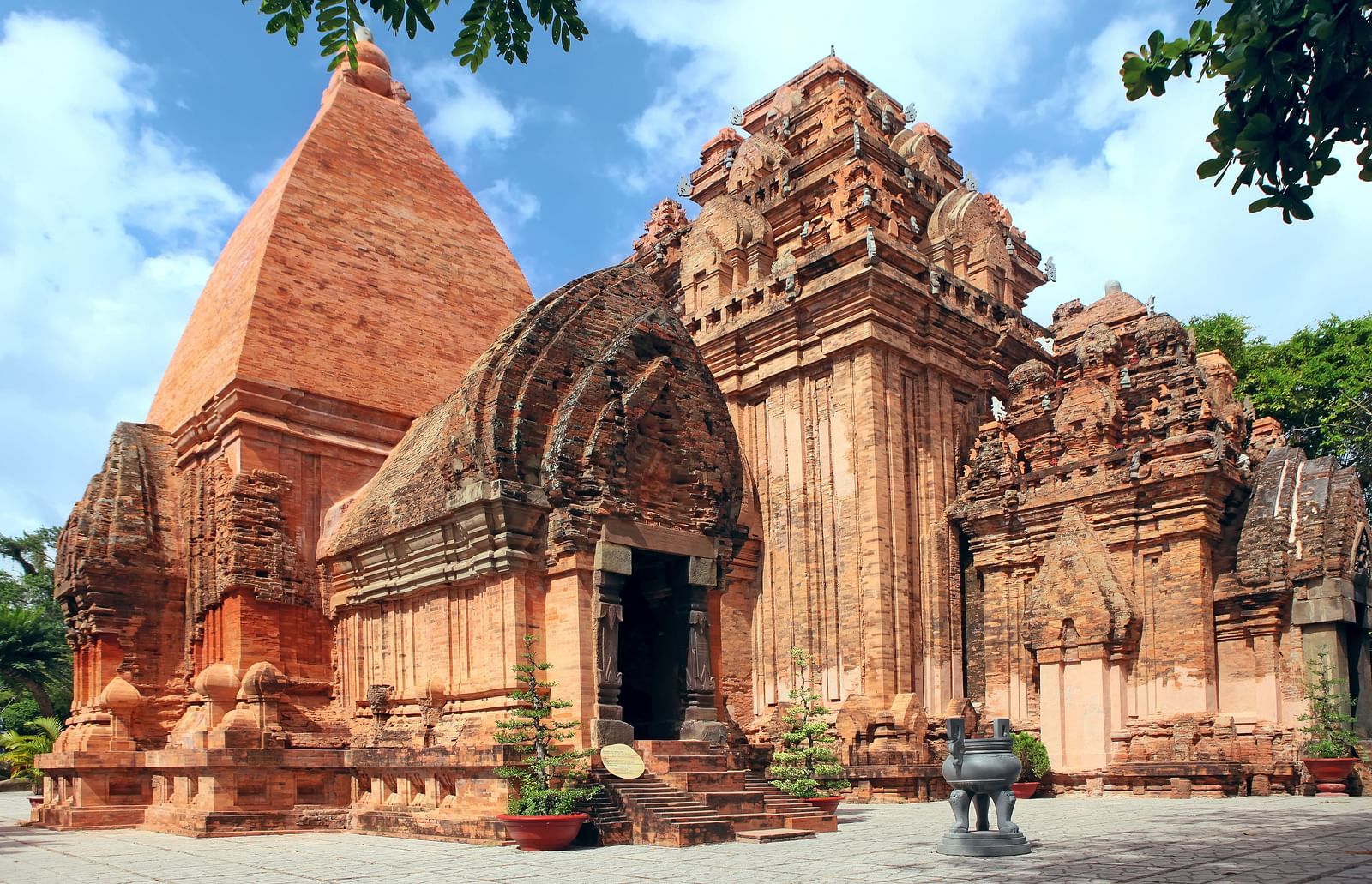 Ancient temple complex with tiered structures and ornate carvings under a partly cloudy sky.
