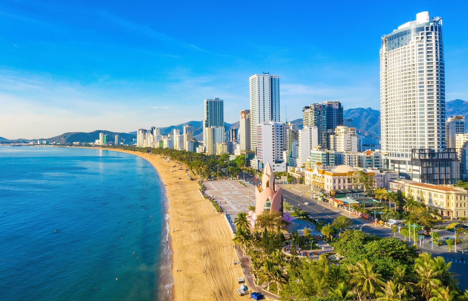 Coastal city view with tall buildings lining a beach, seen from an elevated perspective.