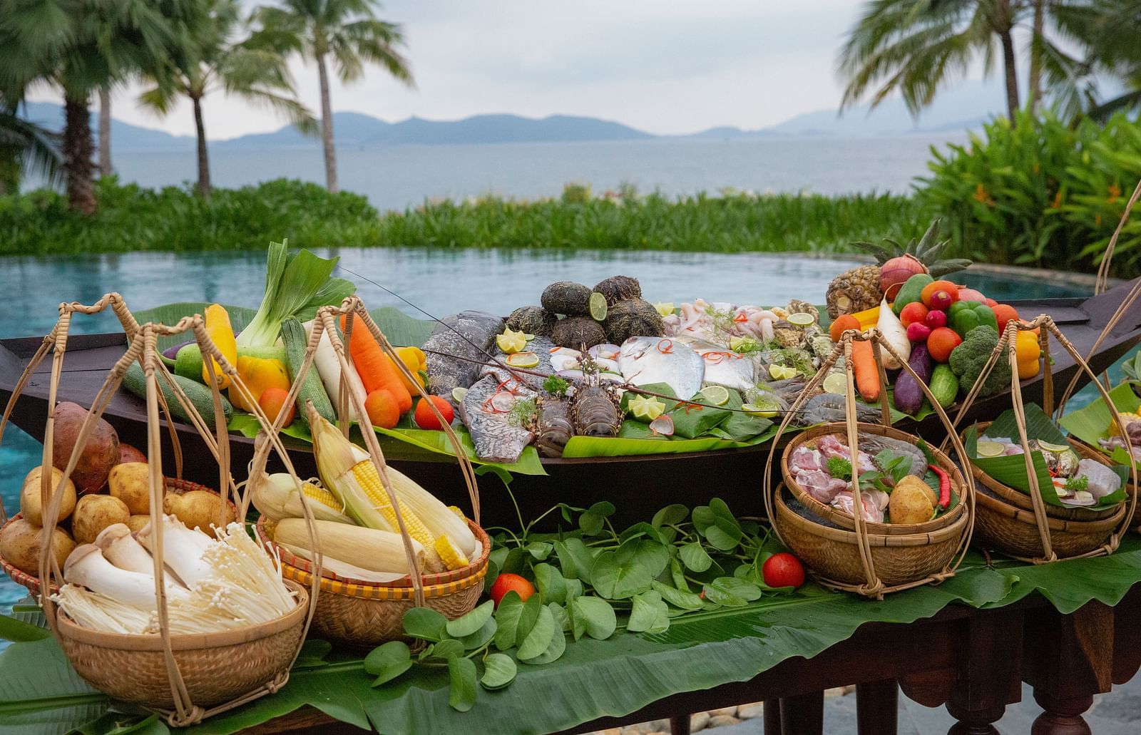 A display of fresh vegetables, fruits, and seafood by the poolside with a scenic background - Alibu Resort Nha Trang, a Beachfront hotel