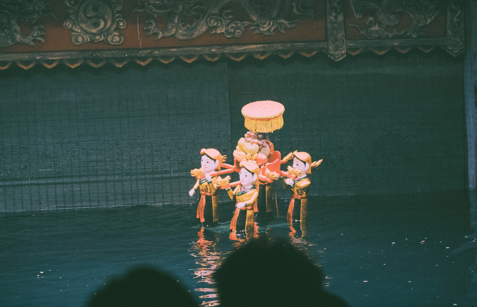 An overview of people dressed as puppets carrying a seat while walking on a waterbody during a Water Puppet Show Nha Trang.