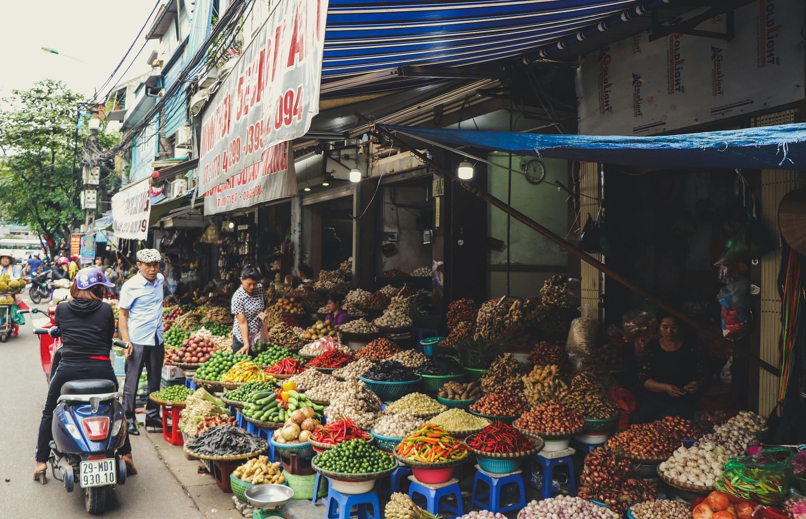 A market with fruits and vegetable stalls with people moving around in Hanoi.