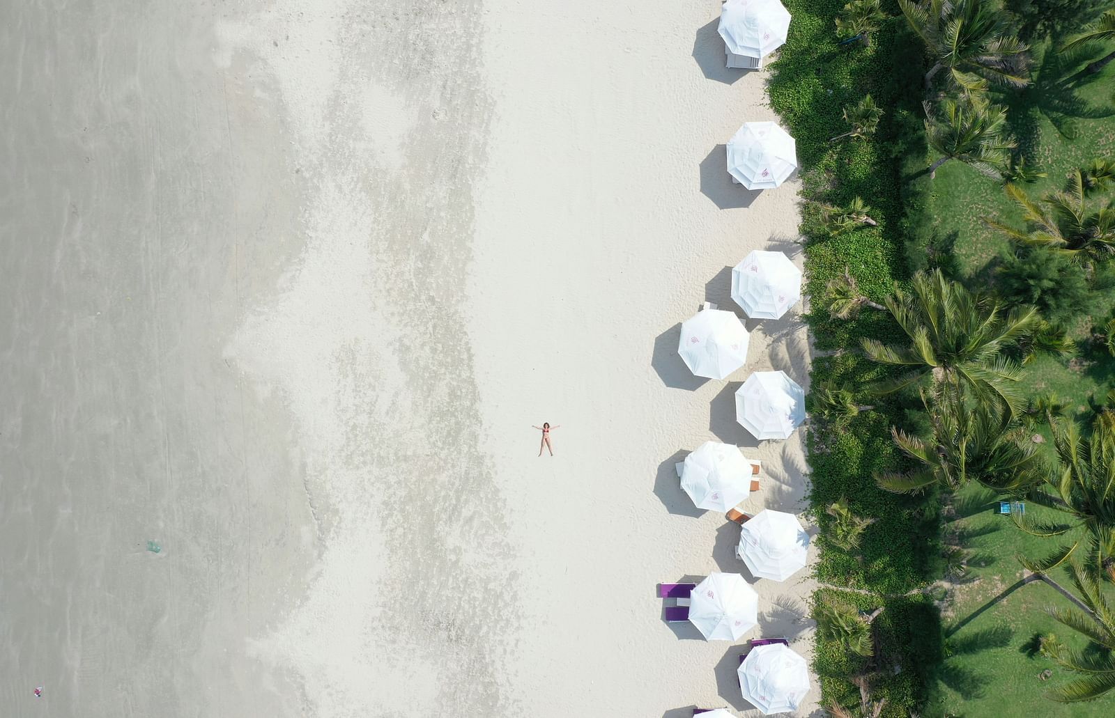 An aerial view of Bãi bi?n D?c L?t Beach with a woman lying down and canopies next to her