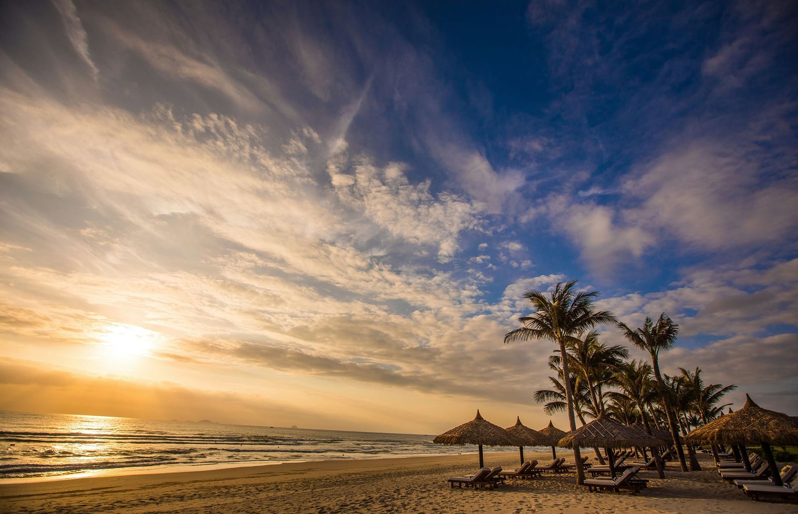 An overview of a beach with canopies in view and sun setting on the left hand side