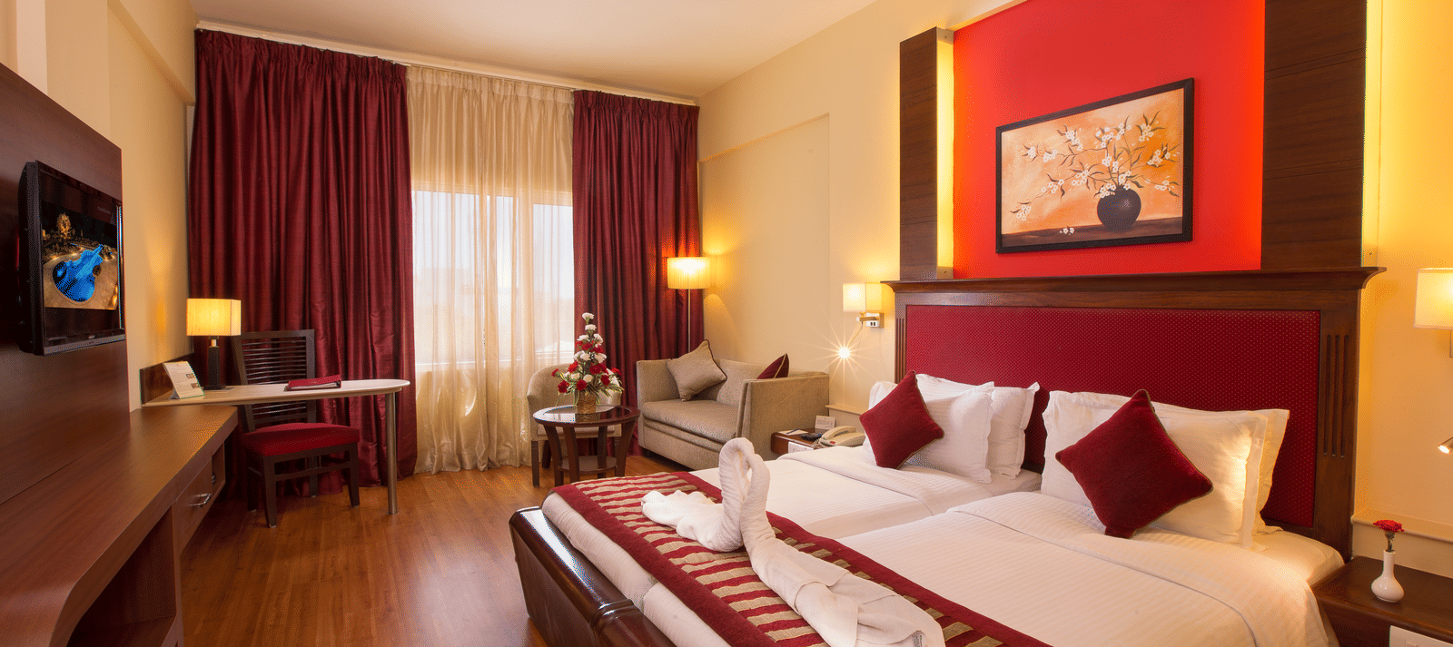 Executive Room at Hotel Atithi featuring a king bed with red accents, warm lighting, a work desk, seating area, and contemporary decor.