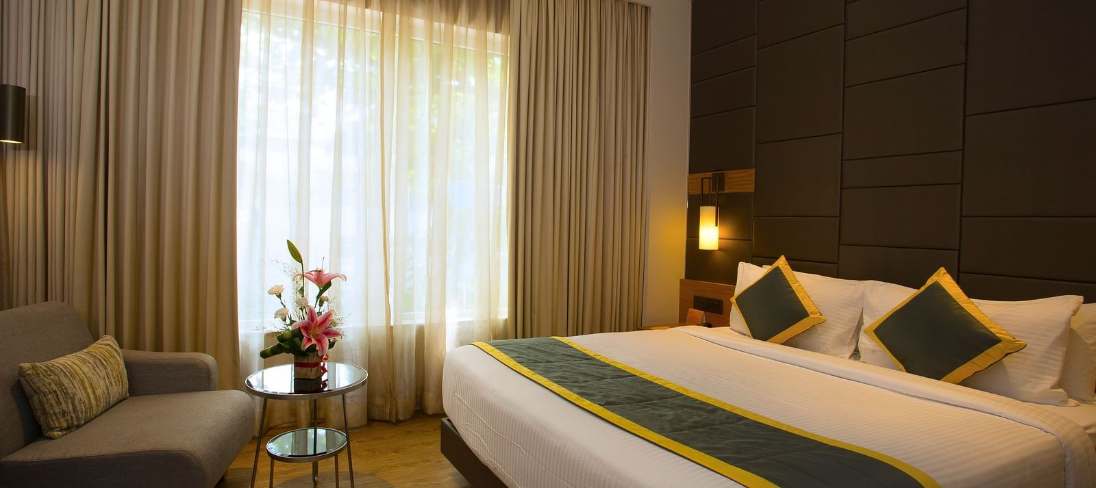 a bedroom with a large bed and a sofa opposite the the bed, with a small table in the middle - Hotel Fountain Tree By TGI - JP Nagar, Bangalore