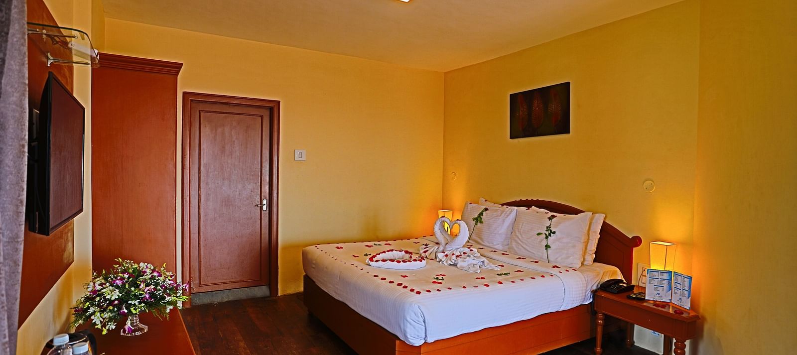 a plush white bed decked with flower petals facing the TV mounted on the wall in a well-lit room and  at La Montana By TGI, Ooty