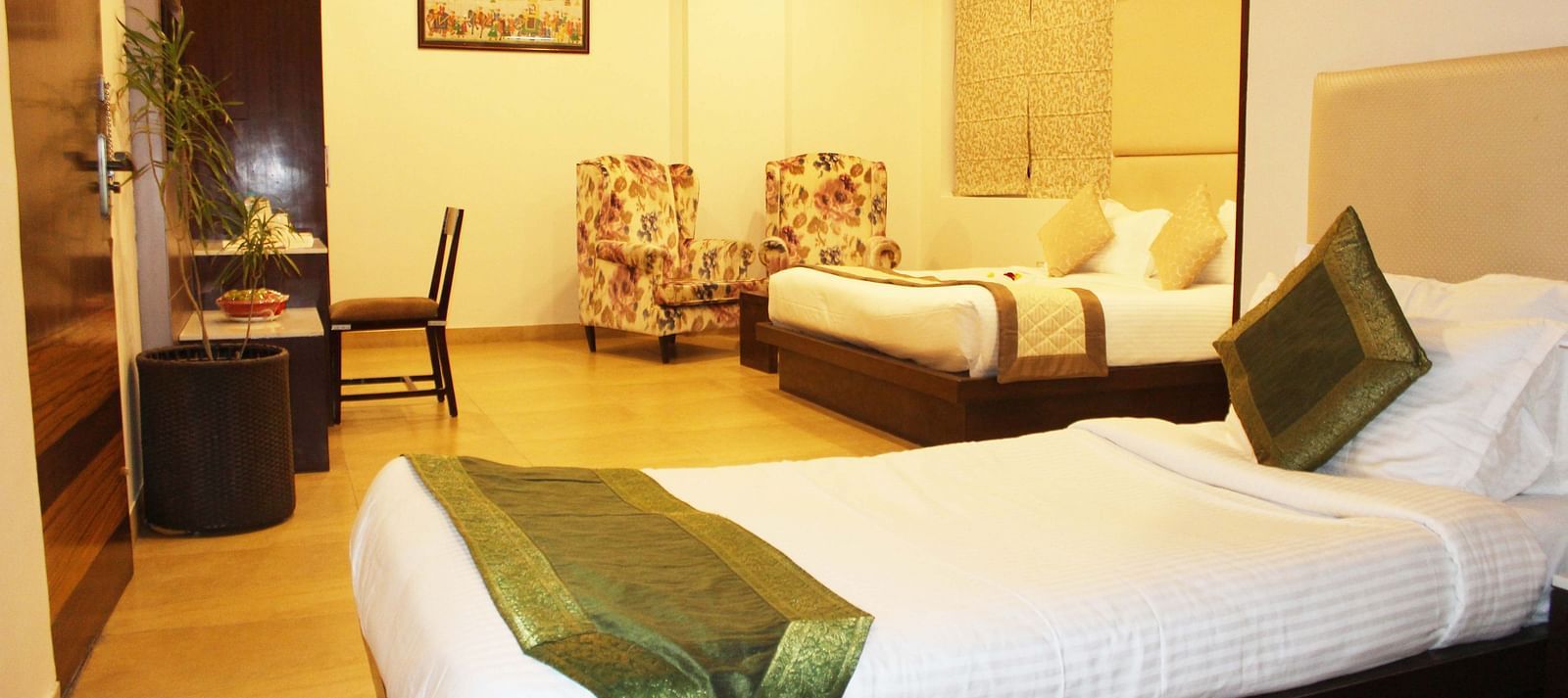 Another view of a spacious hotel room with two armchairs, a large bed with white linens and patterned wallpaper - TGI Apple Inn, Jaipur 