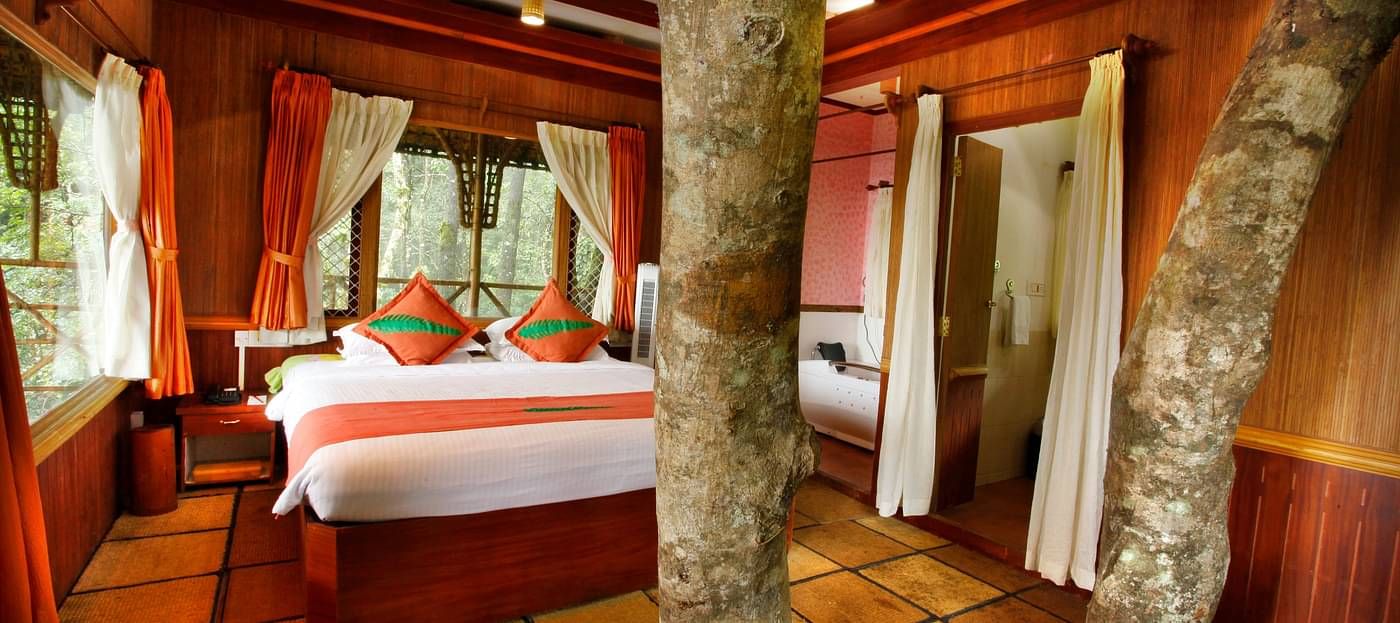 Room with a bed and tree trunks protruding out of the floor at Vythiri Resort, Wayanad
