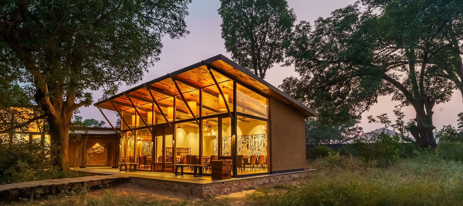 Facade view of a well lit cottage surrounded by trees at Trees N Tigers, Tadoba.