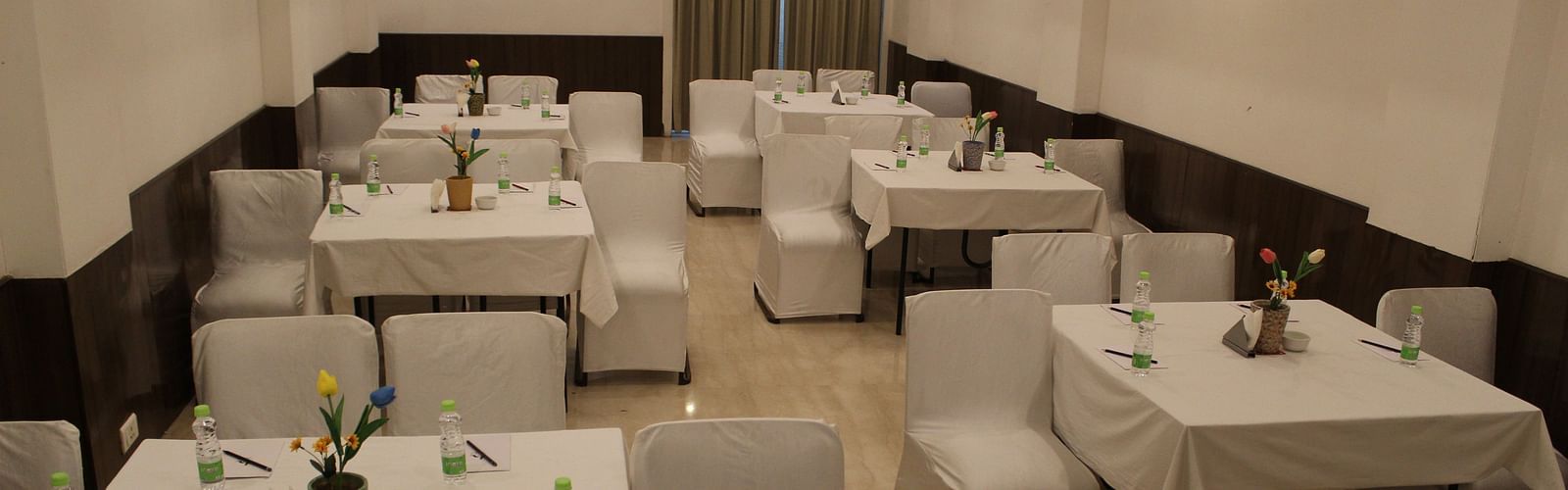 An image of a banquet hall at Inde Hotel Vista Woods featuring a few sets of tables with four chairs each