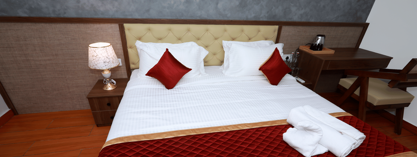 A close-up shot of the double bed at the Standard Room with a maroon bed runner along with white towels kept over it at WOW Naturefull Resorts, Yercaud.
