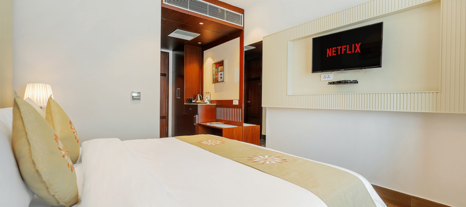 A hotel bedroom featuring a bed with a light green runner, a plush headboard, and a wall-mounted television screen at BluSalzz Select City Centre, Amritsar.